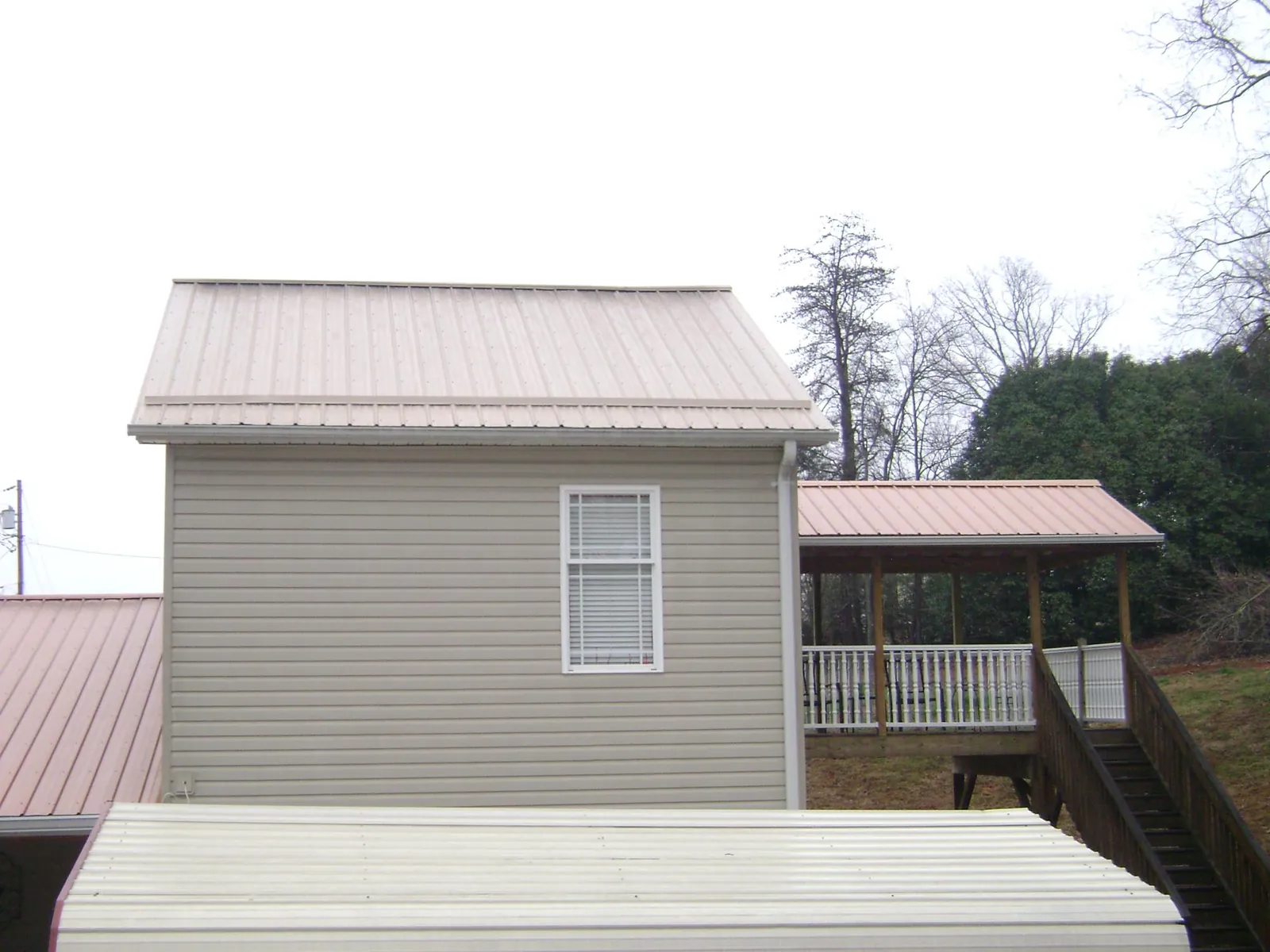 Tan metal roofs on a two story addition and attached porch, from a Roof Replacement job in Saint Joseph